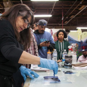 Women works with ink on a print while doing a demonstration in front of several people.